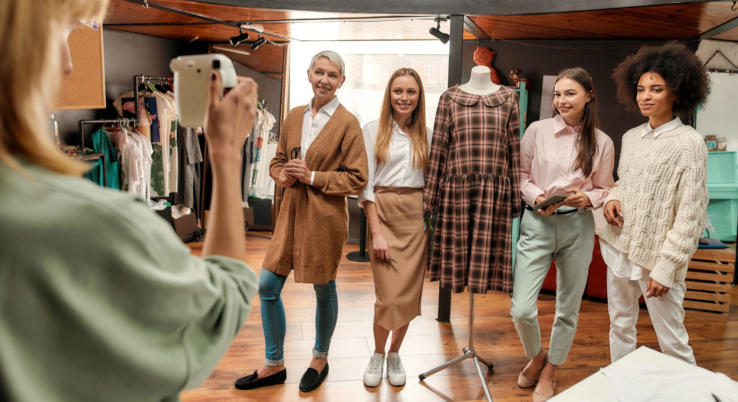 Portrait d'un groupe de femmes avec au milieu un mannequin de couture qui porte une robe à carreaux. On voit de dos la photographe qui prend la photo